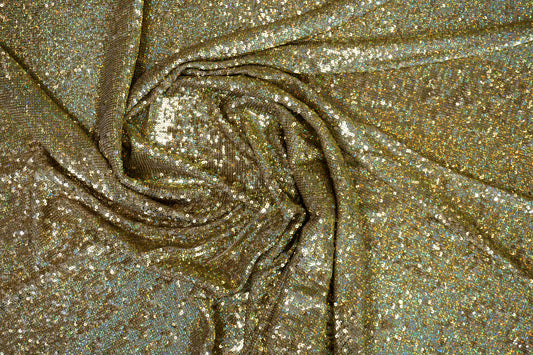 Luxuriöser Paillettenstoff in Gold mit irisierendem Regenbogeneffekt auf hellem Nude-Tüll