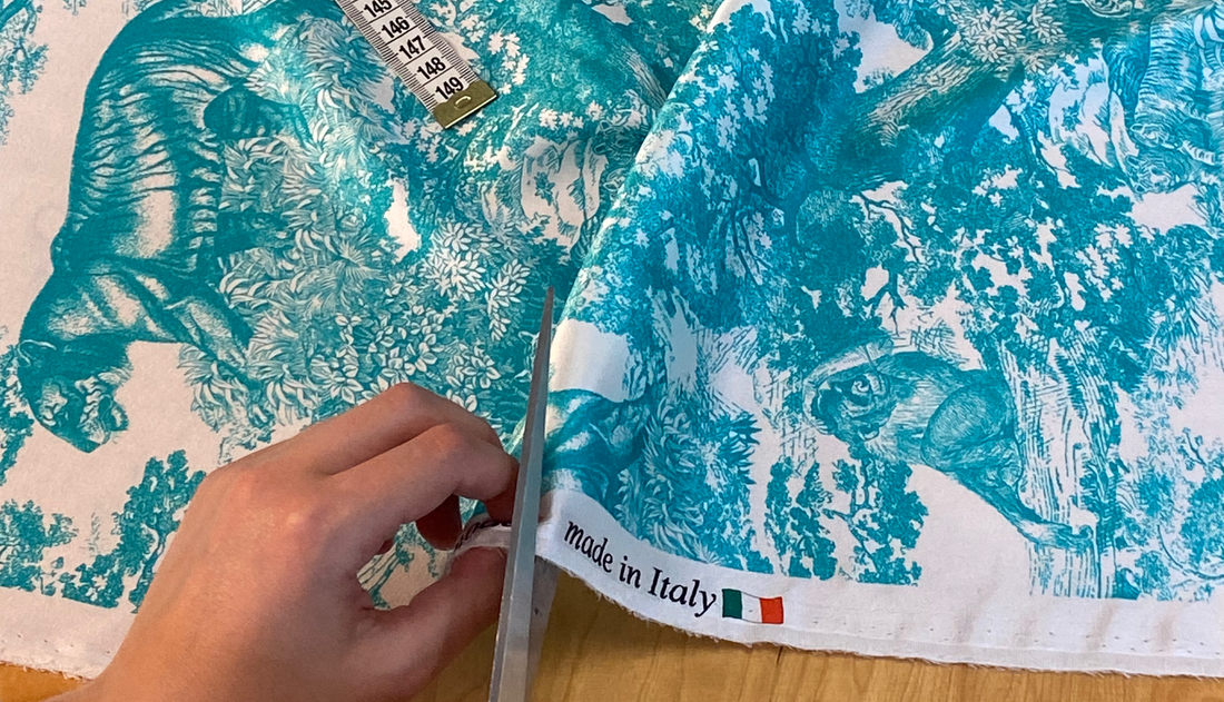ein weißer Seidensatin mit Türkisen Tiger-print und Webkante mit "made in Italy" wird von einer Hand mit Schere geschnitten. 