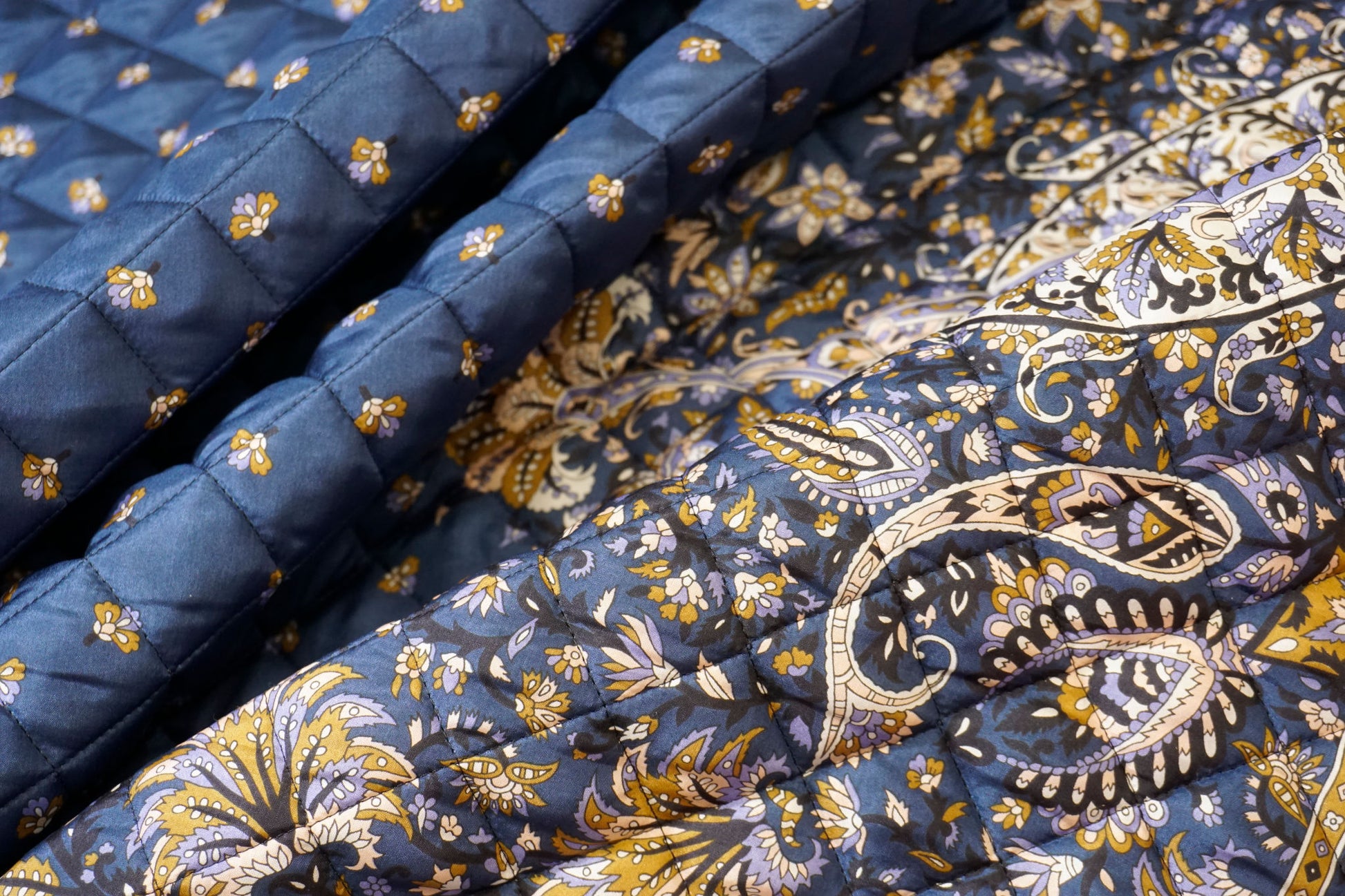 Detailaufnahme des Steppstoffs – feine Rautensteppung, seidige Oberfläche und filigrane goldene Blütenakzente